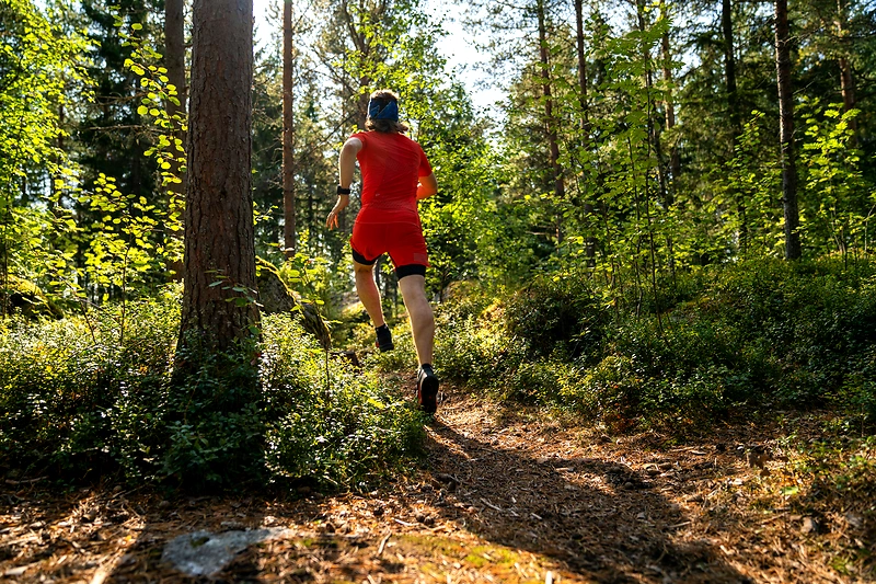Löpare i gul tröja springer i terräng vid sjö. Kolmårdsrundan trail run.